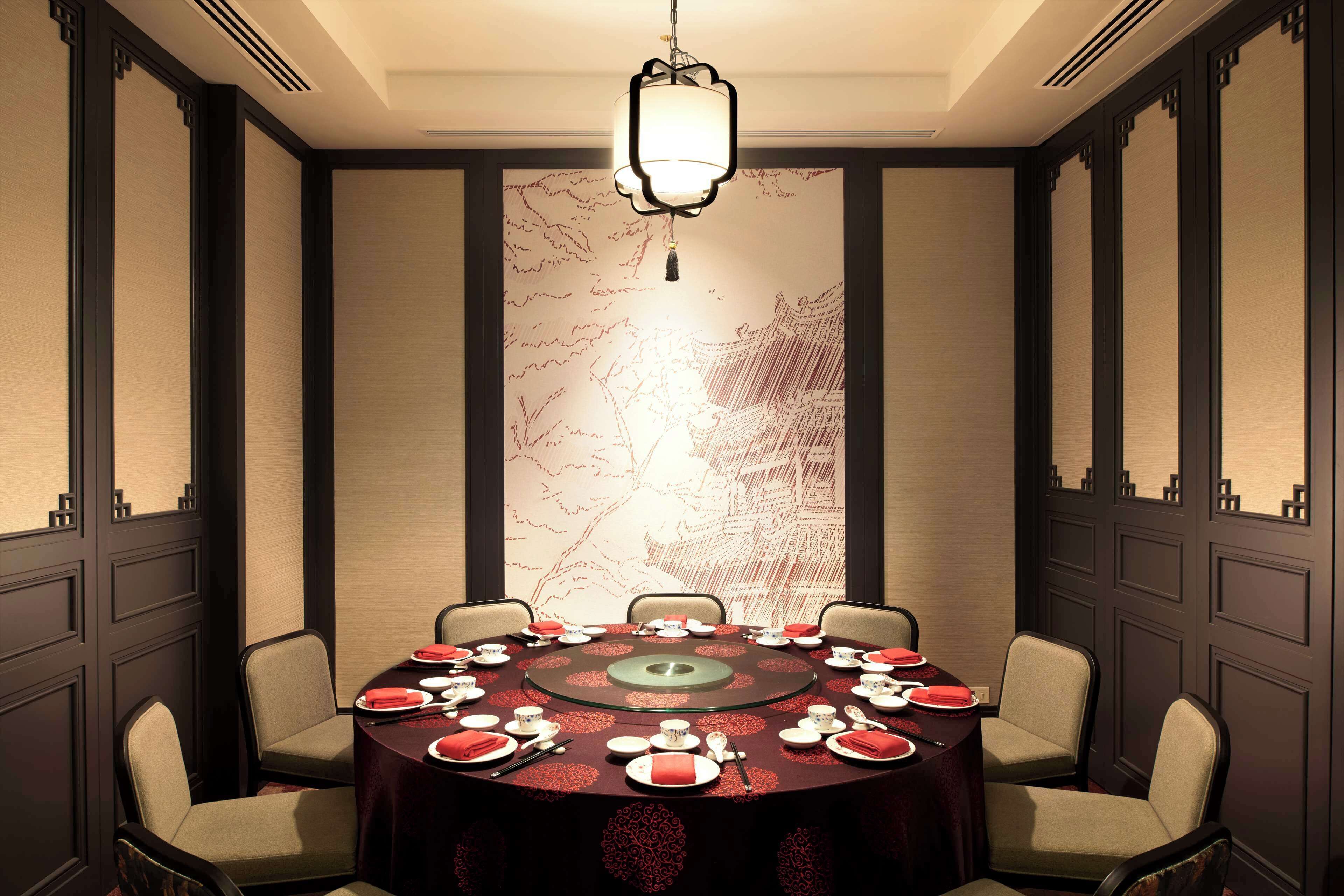 A conference room with a round table set for a meeting, surrounded by chairs, with a decorative wall and a hanging light fixture.