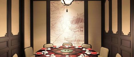 A conference room with a round table set for a meeting, surrounded by chairs, with a decorative wall and a hanging light fixture.