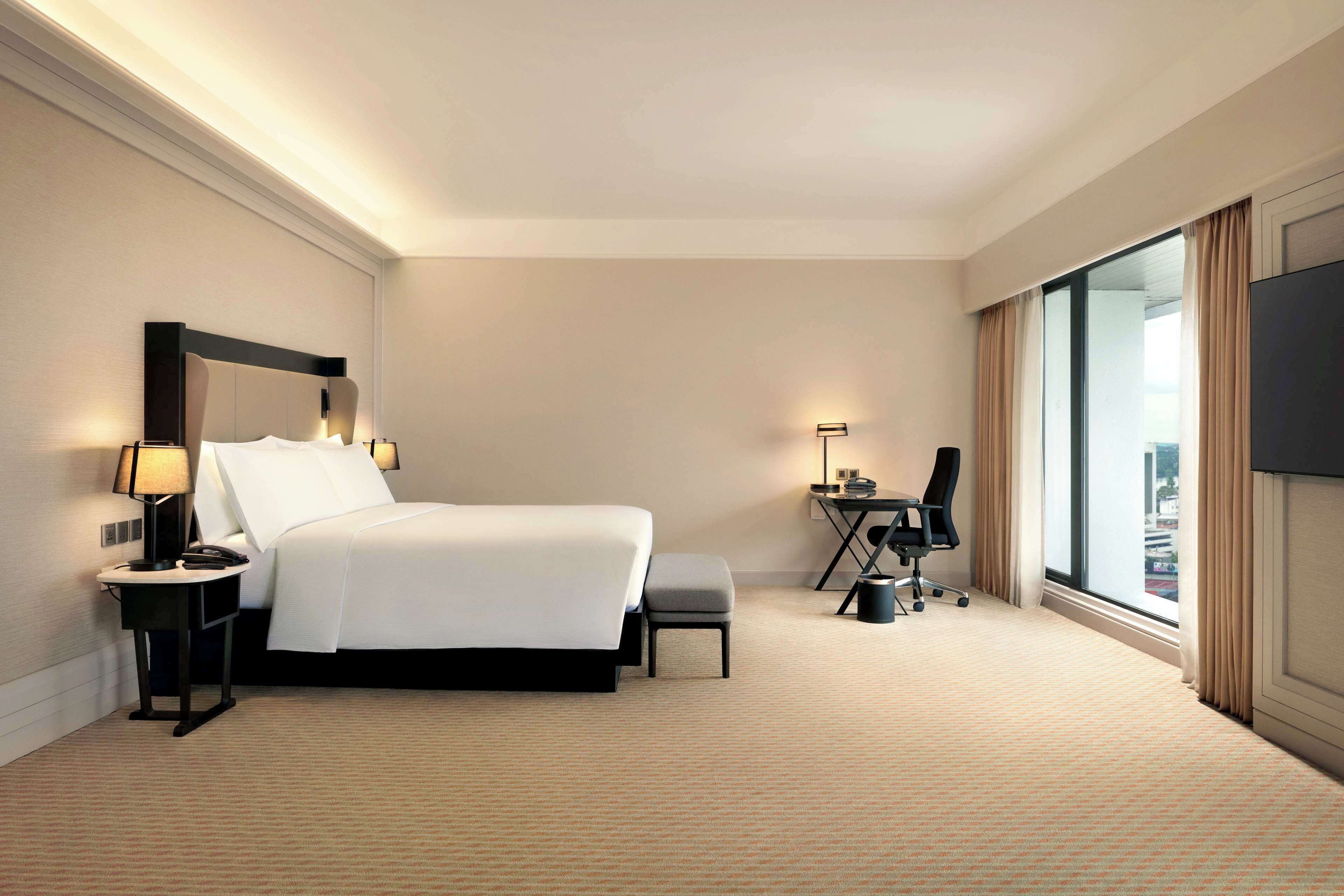 A hotel room with a large bed, a desk, a chair, a TV, and a window with curtains.