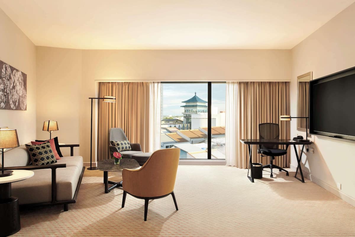 A hotel room with a large window, a sofa, a chair, a desk, a TV, and a lamp.