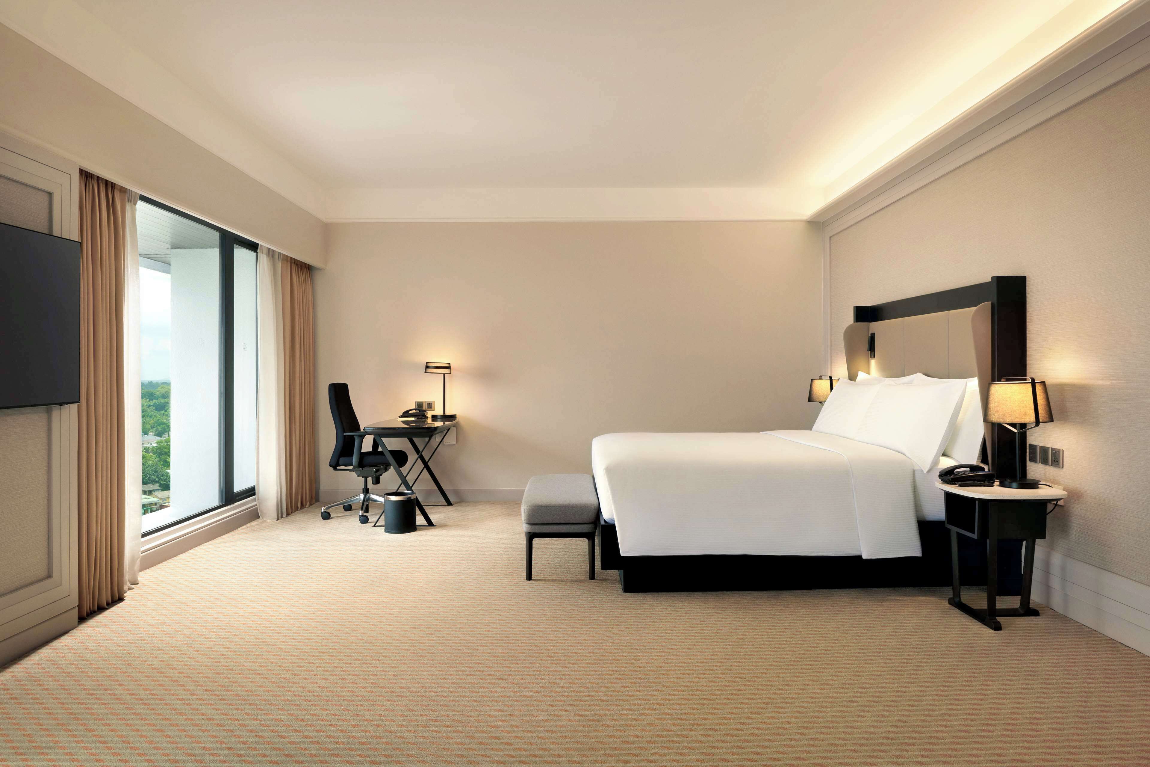 A hotel room with a large bed, a desk with a chair, a small table, a nightstand, and a TV.