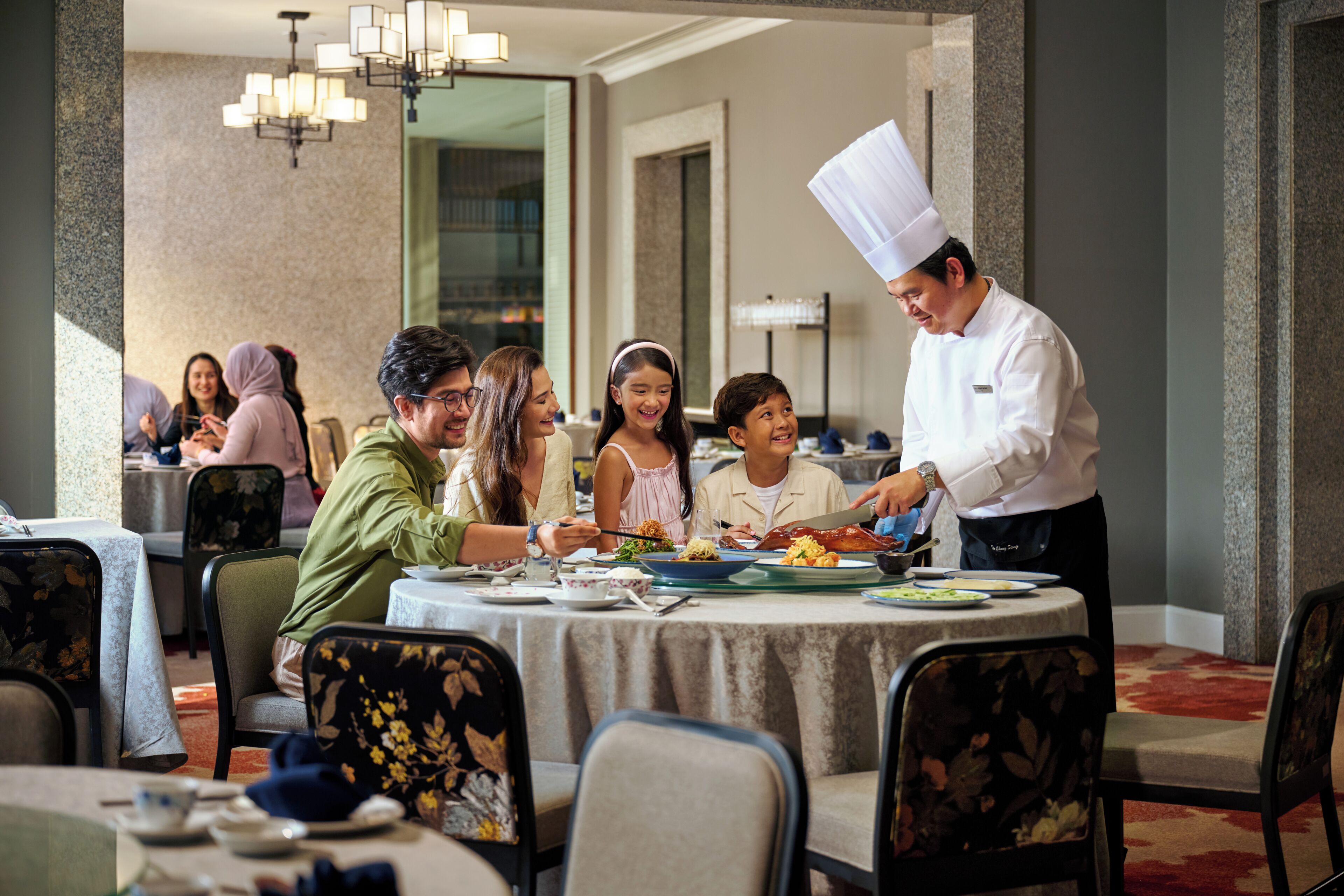 A dining area with round tables, chairs, and a chef serving food.