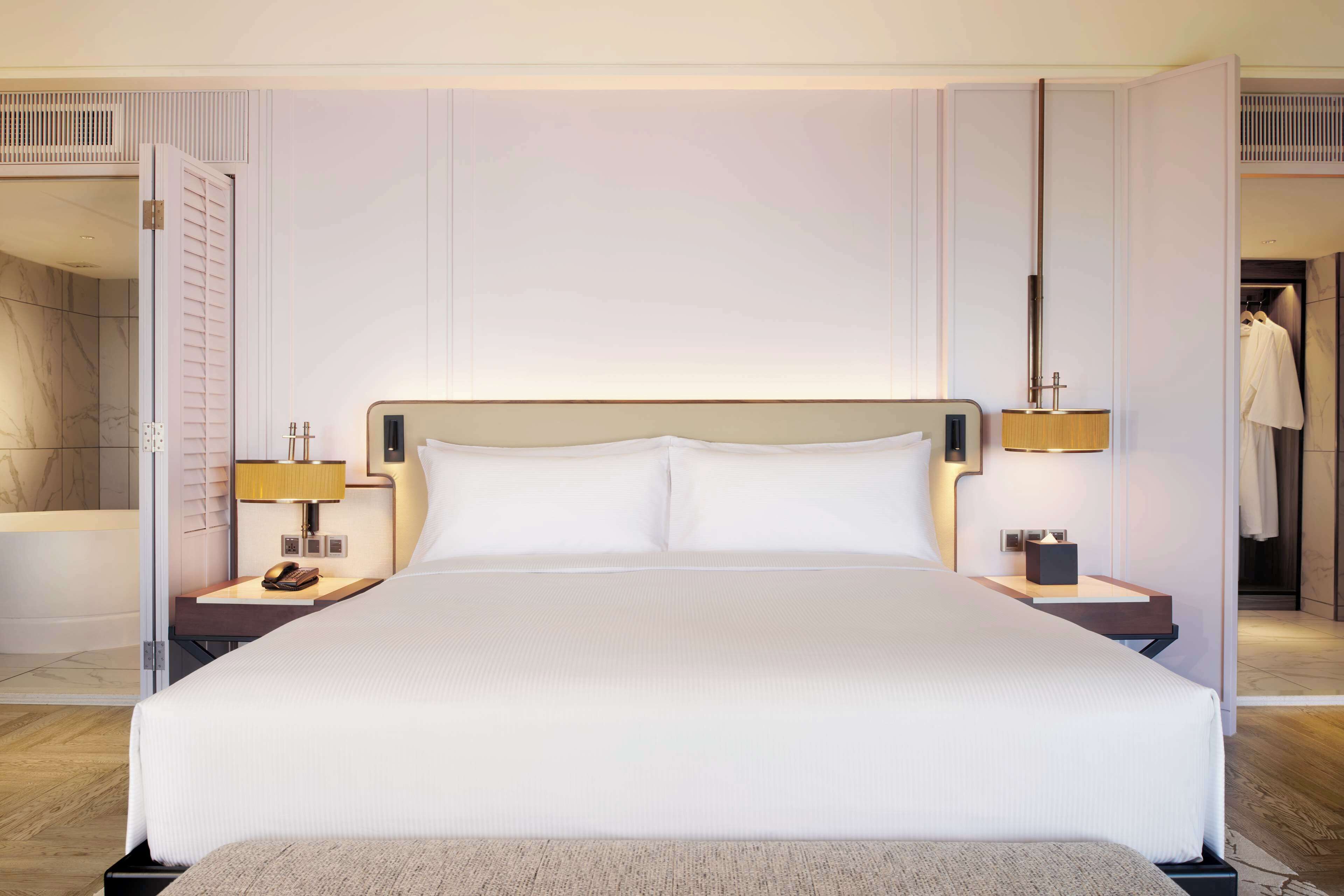 A large bed with white linens, two bedside tables with lamps, and a mirror above the bed.