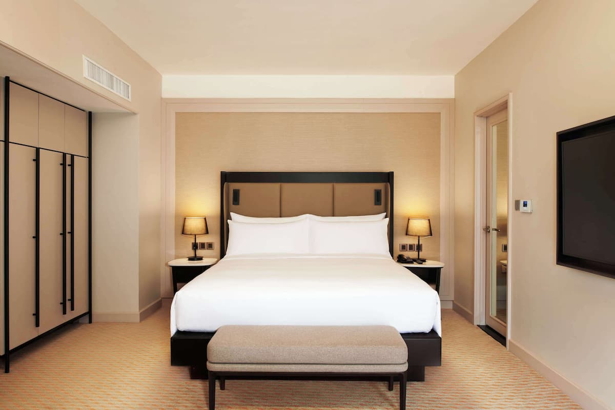 A hotel room with a large bed, bedside lamps, a TV, a wardrobe, and a bench.