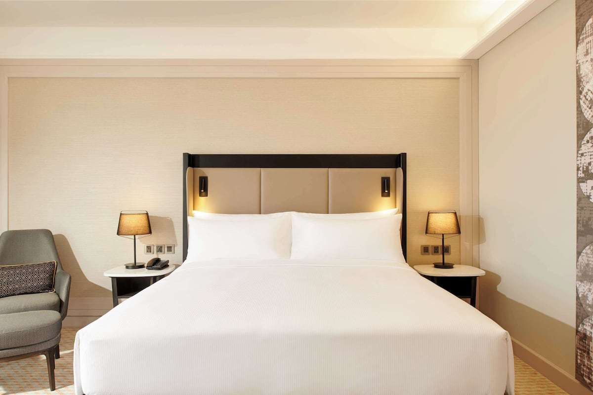 A hotel room with a large bed, two bedside tables with lamps, a chair, and a wall with a patterned design.