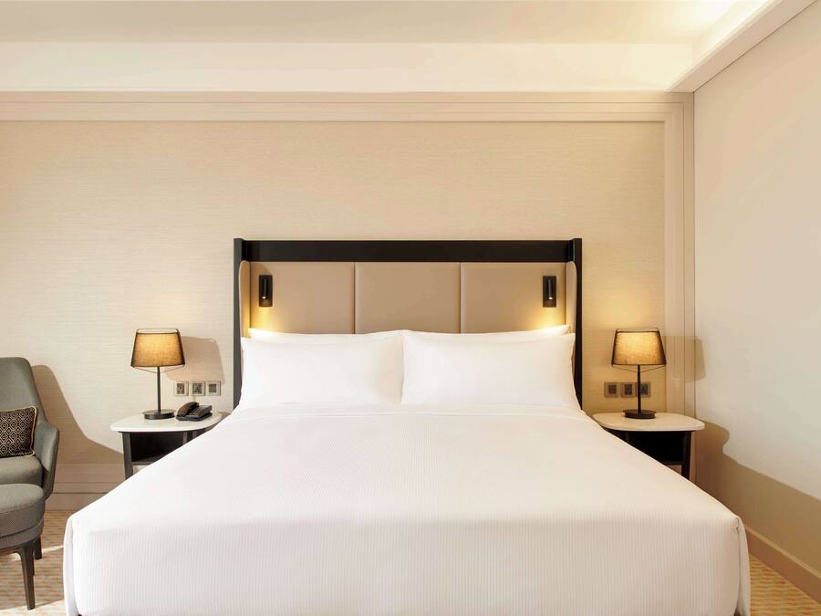A hotel room with a large bed, two bedside tables with lamps, a chair, and a wall with a patterned design.