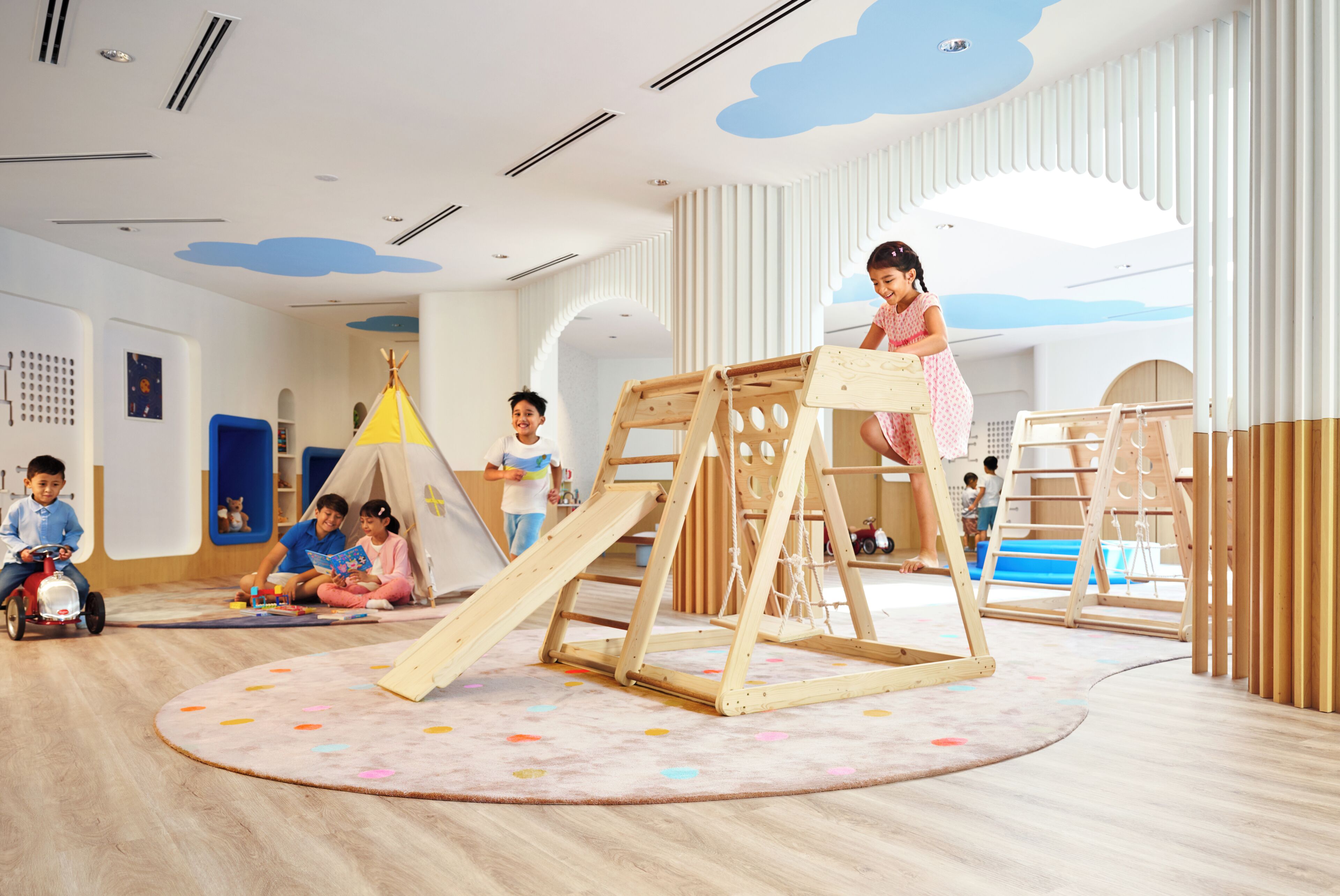 Ein Kinderspielzimmer mit einer Holzspielkonstruktion, einem Zelt und einem Rundteppich mit Muster.