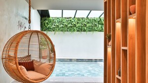 Una silla colgante con cojines, una piscina con azulejos y un estante de madera con adornos.