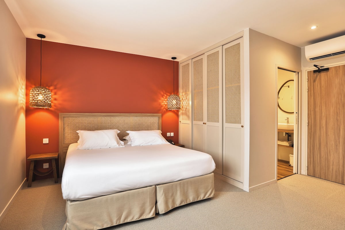 A bedroom with a bed, bedside lamps, a wardrobe, and an air conditioning unit.