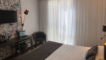 A hotel room with a bed, a desk, a chair, a TV, and a window with curtains.