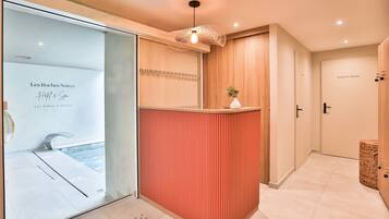 Un área de recepción con mostrador de madera, lámpara colgante y puerta de vidrio que da a una piscina.