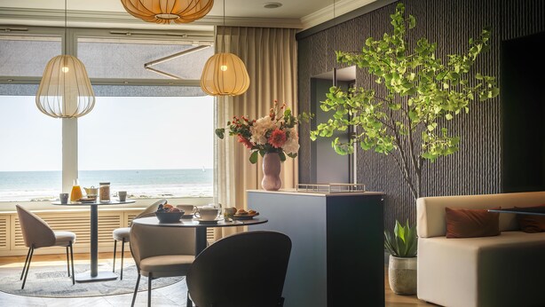 Habitación de hotel moderna con comedor, sofá y vistas al océano.