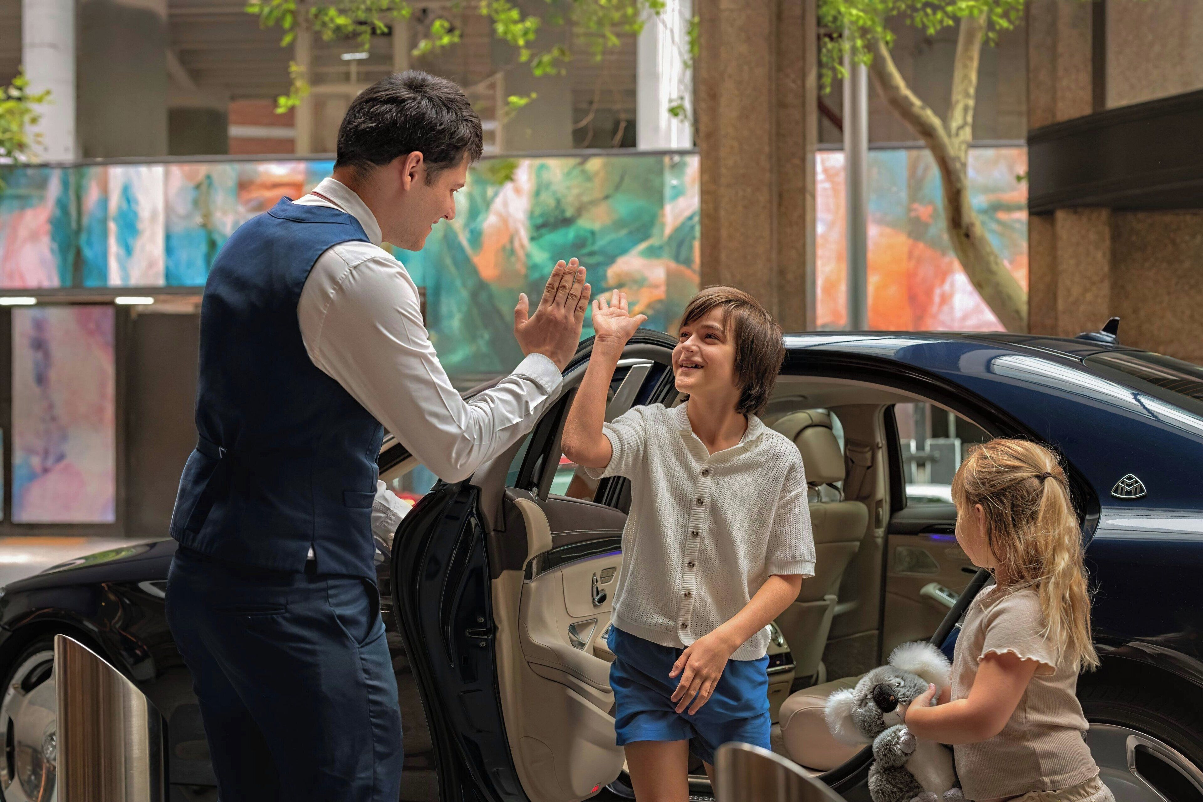 A man giving a high-five to a child in a car, with another child sitting in the back.