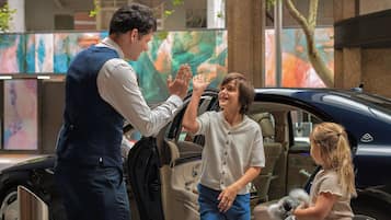 A man giving a high-five to a child in a car, with another child sitting in the back.