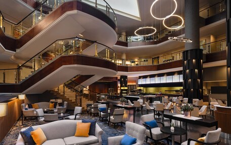 A multi-level hotel lobby with a central staircase, seating areas, and a bar.