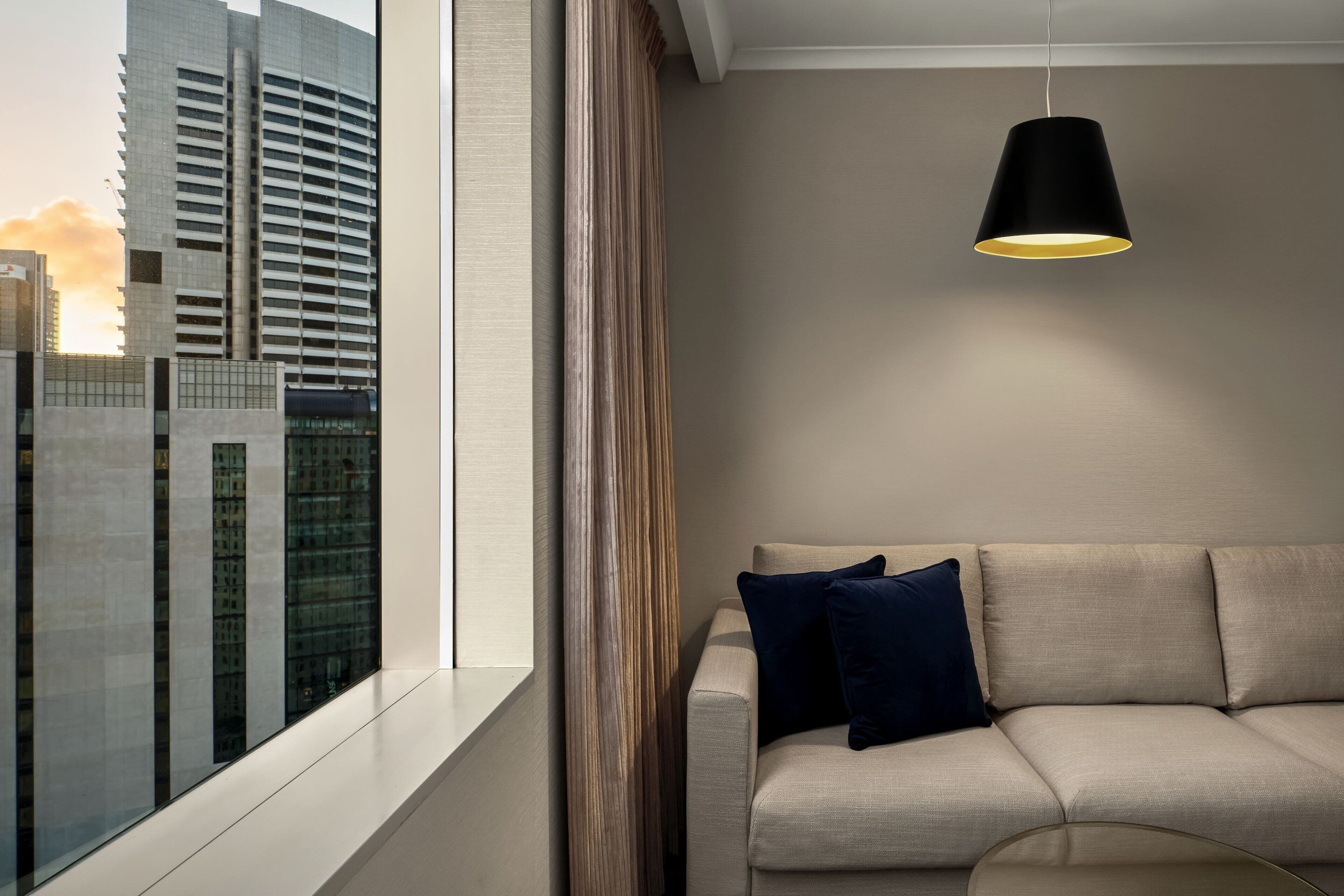 Ett modernt vardagsrum med en soffa, en hängande lampa och utsikt över en stadssiluett genom ett stort fönster.