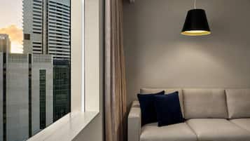 Una sala de estar moderna con un sofá, una lámpara colgante y vistas a un paisaje urbano a través de un amplio ventanal.