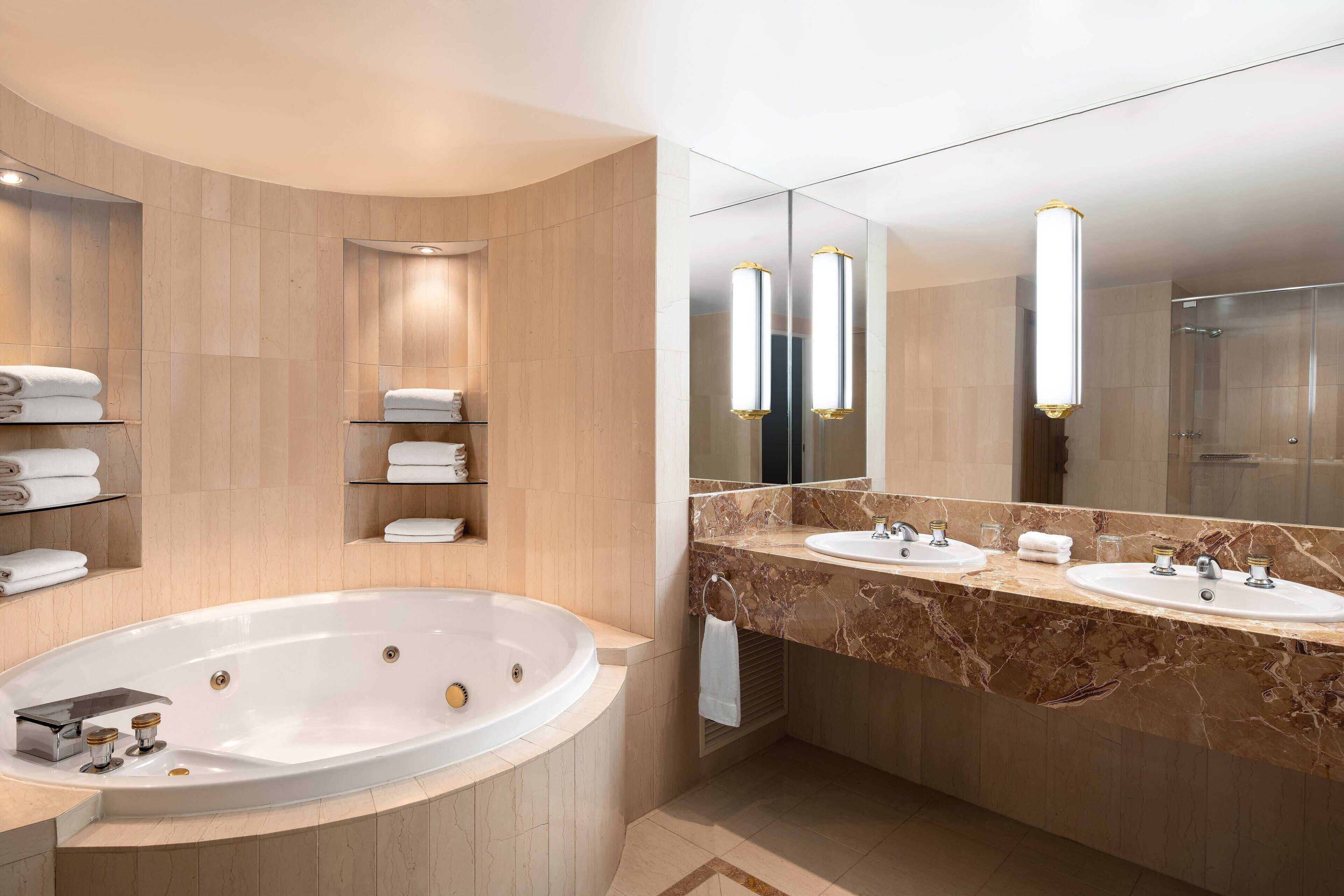 A modern bathroom with a large freestanding bathtub, two sinks, and a large mirror.