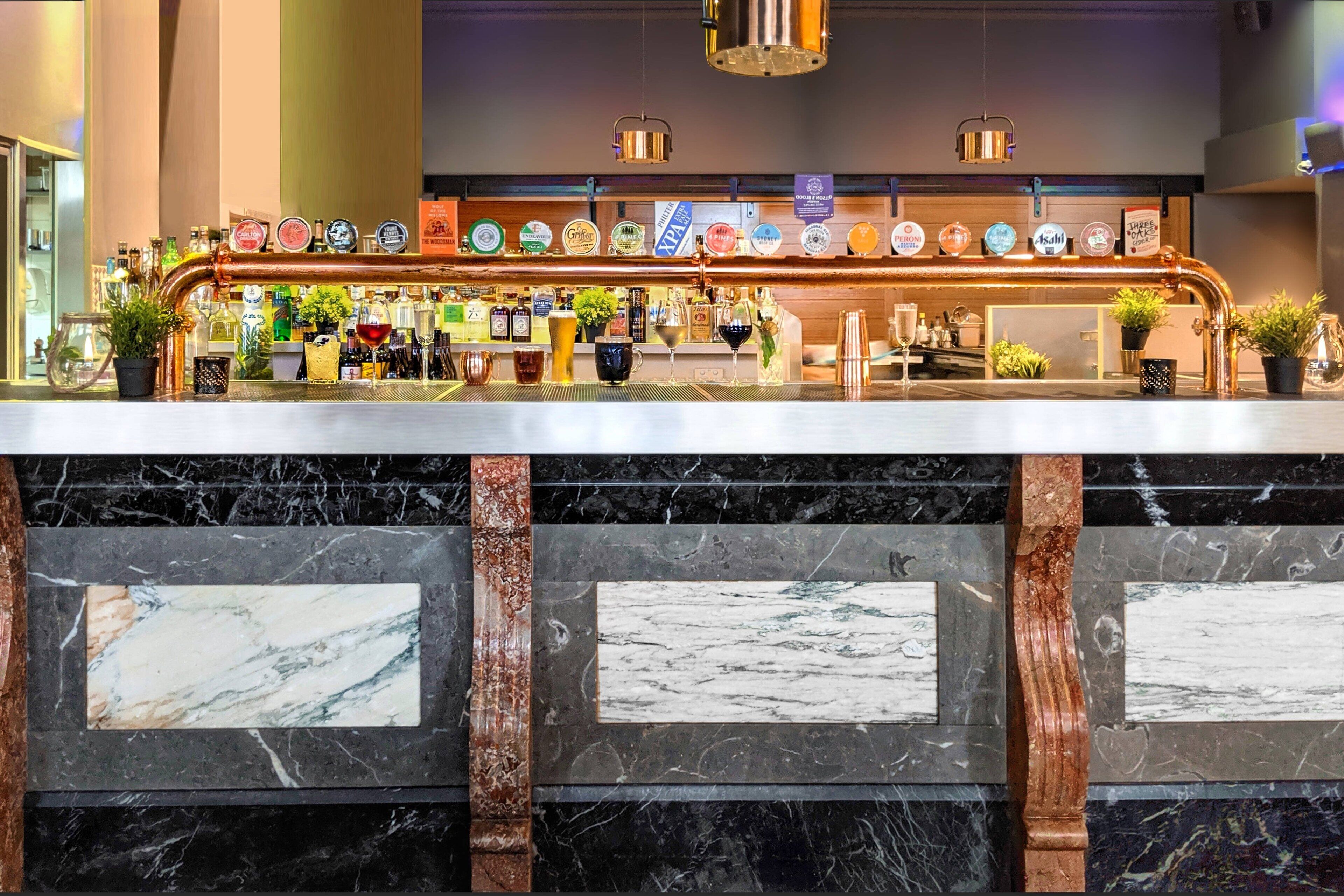 A bar area with a copper beer tap system, various bottles, and glasses on shelves.