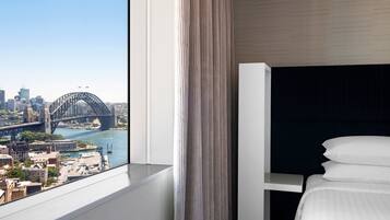Habitación de hotel con cama, ventana con cortinas y vista a un paisaje urbano que incluye un puente.