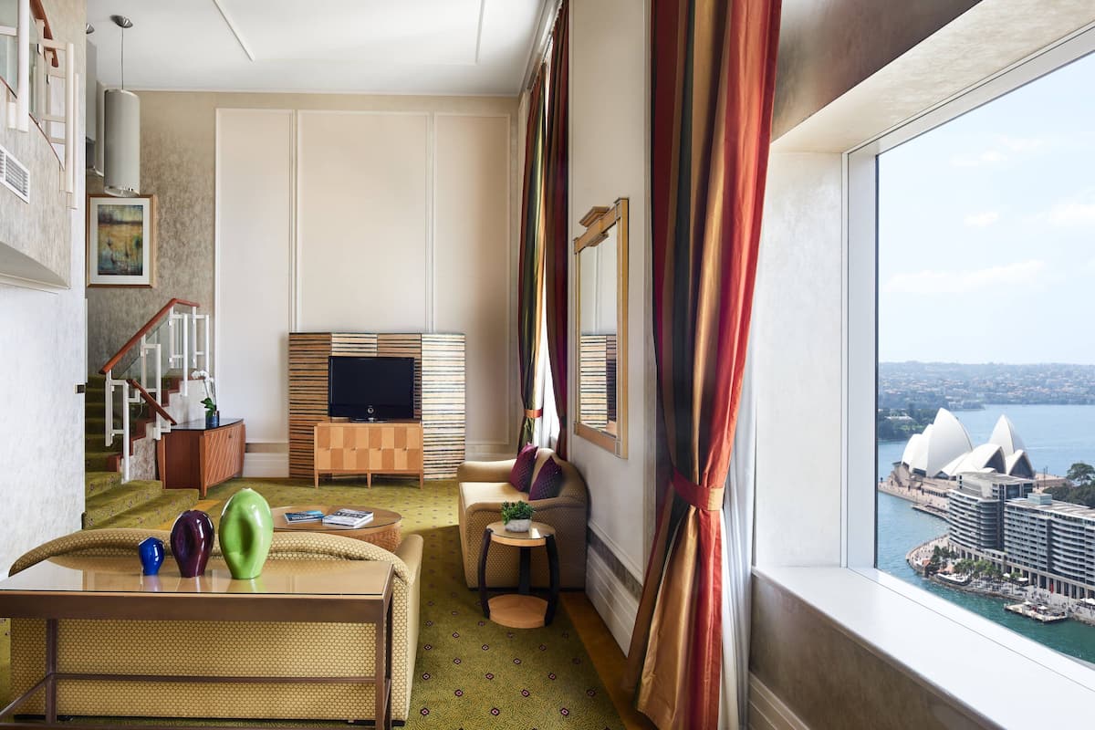 A hotel room with a view of the Sydney Opera House, a sofa, a small table with decorative items, and a television.