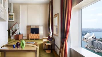 A hotel room with a view of the Sydney Opera House, a sofa, a small table with decorative items, and a television.