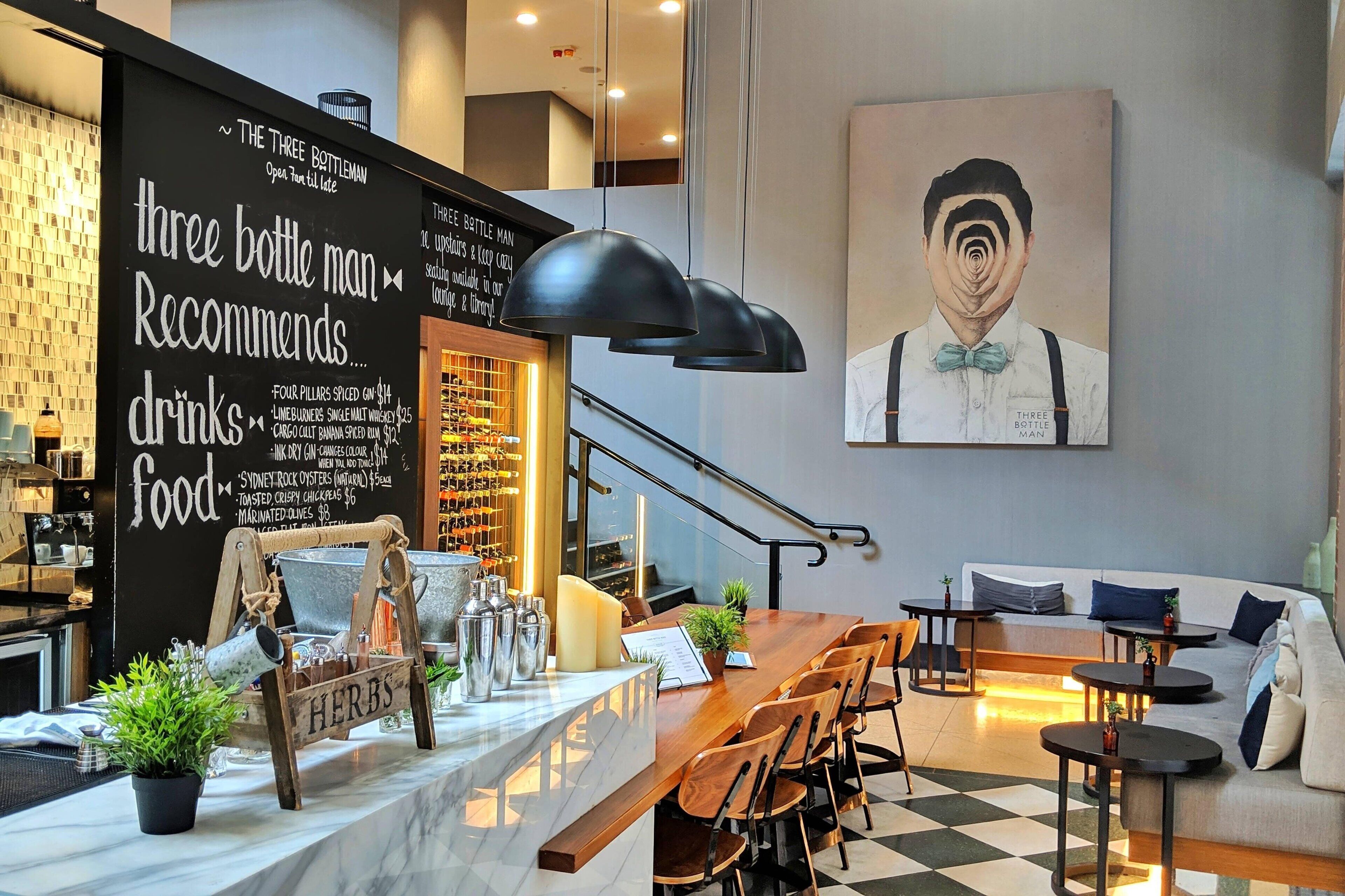 Interior de una cafetería moderna con un menú en pizarra, muebles de madera y un cuadro grande en la pared.