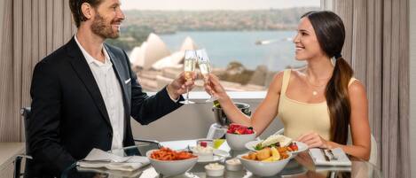 A man and woman toasting with champagne glasses at a table with a view of Sydney Opera House.
