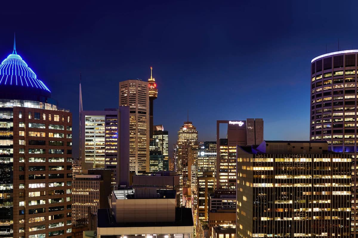 A cityscape at night with illuminated buildings, including a prominent tower with a spire and a dome with blue lights.