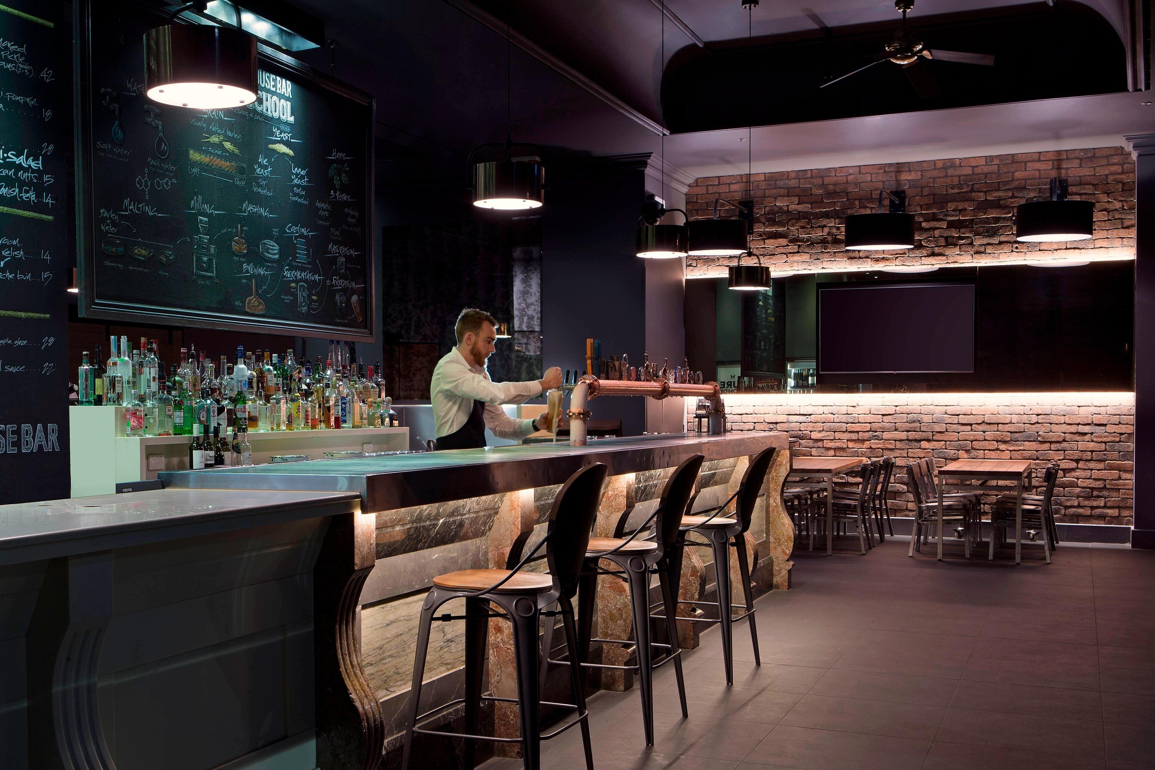 A bar area with a chalkboard menu, bar stools, and a bartender.