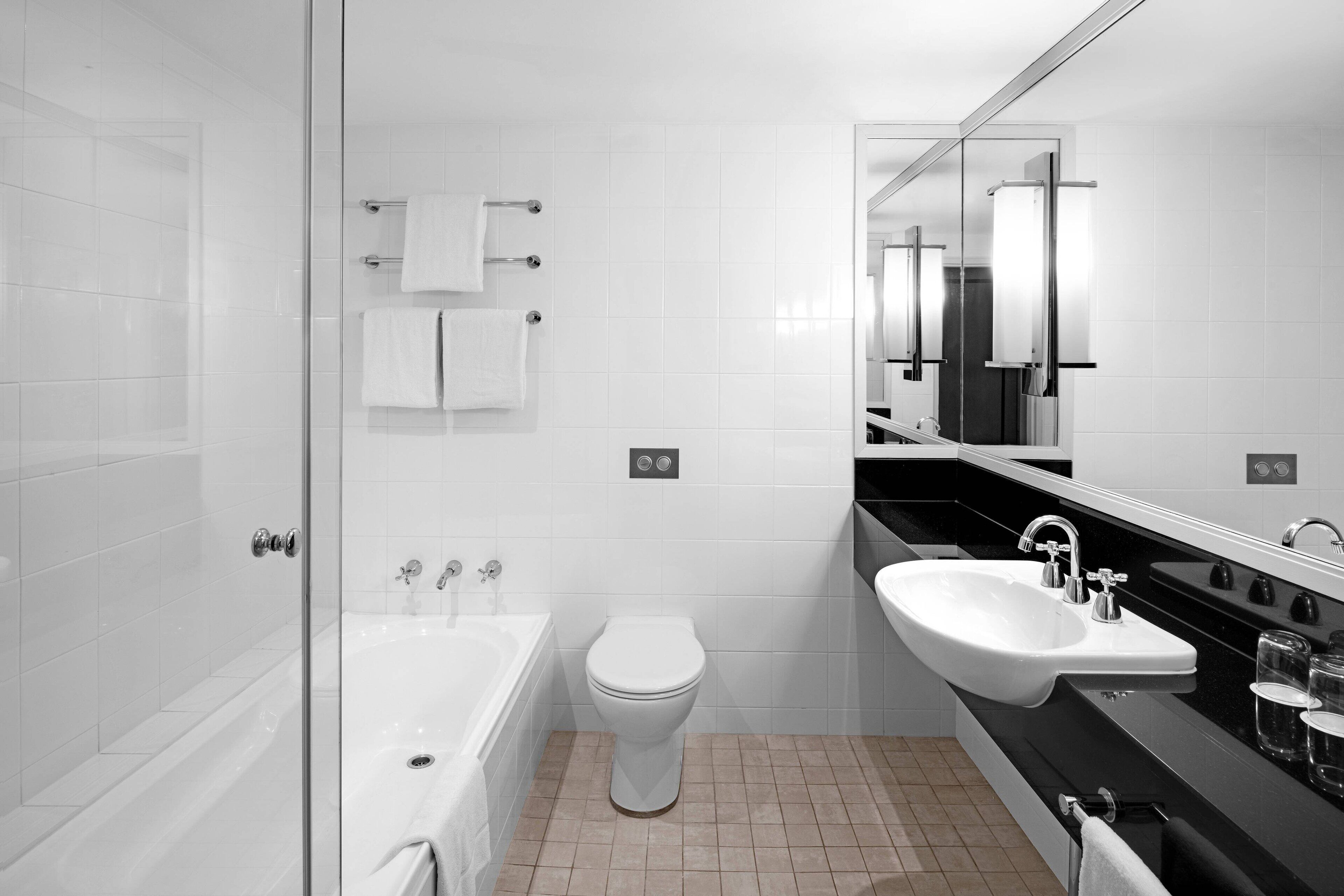 A modern bathroom with a glass shower enclosure, a white toilet, a bathtub, and a black sink with a mirror above it.