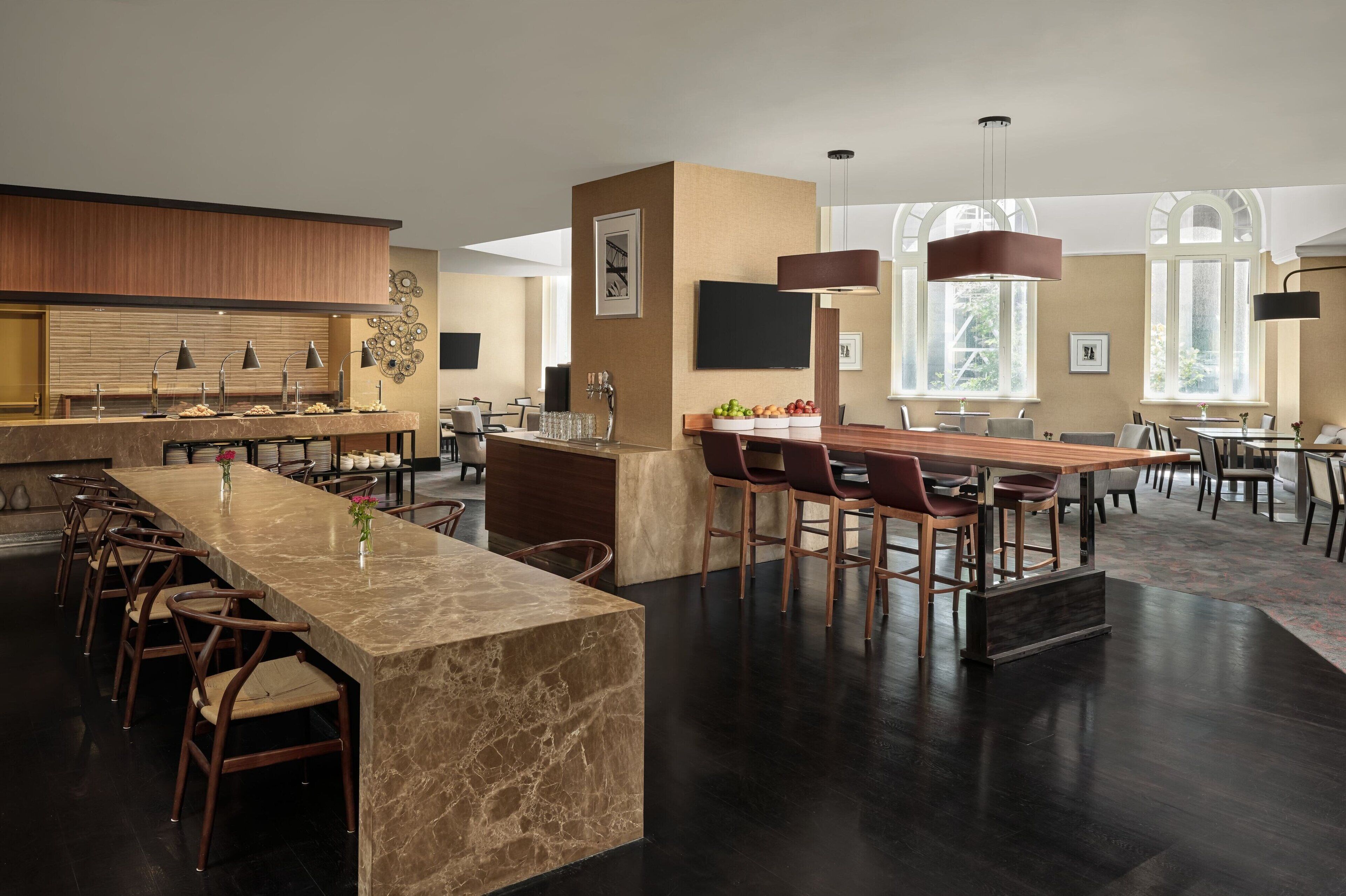 A modern hotel lobby with a marble reception desk, multiple seating areas, and large windows providing natural light.
