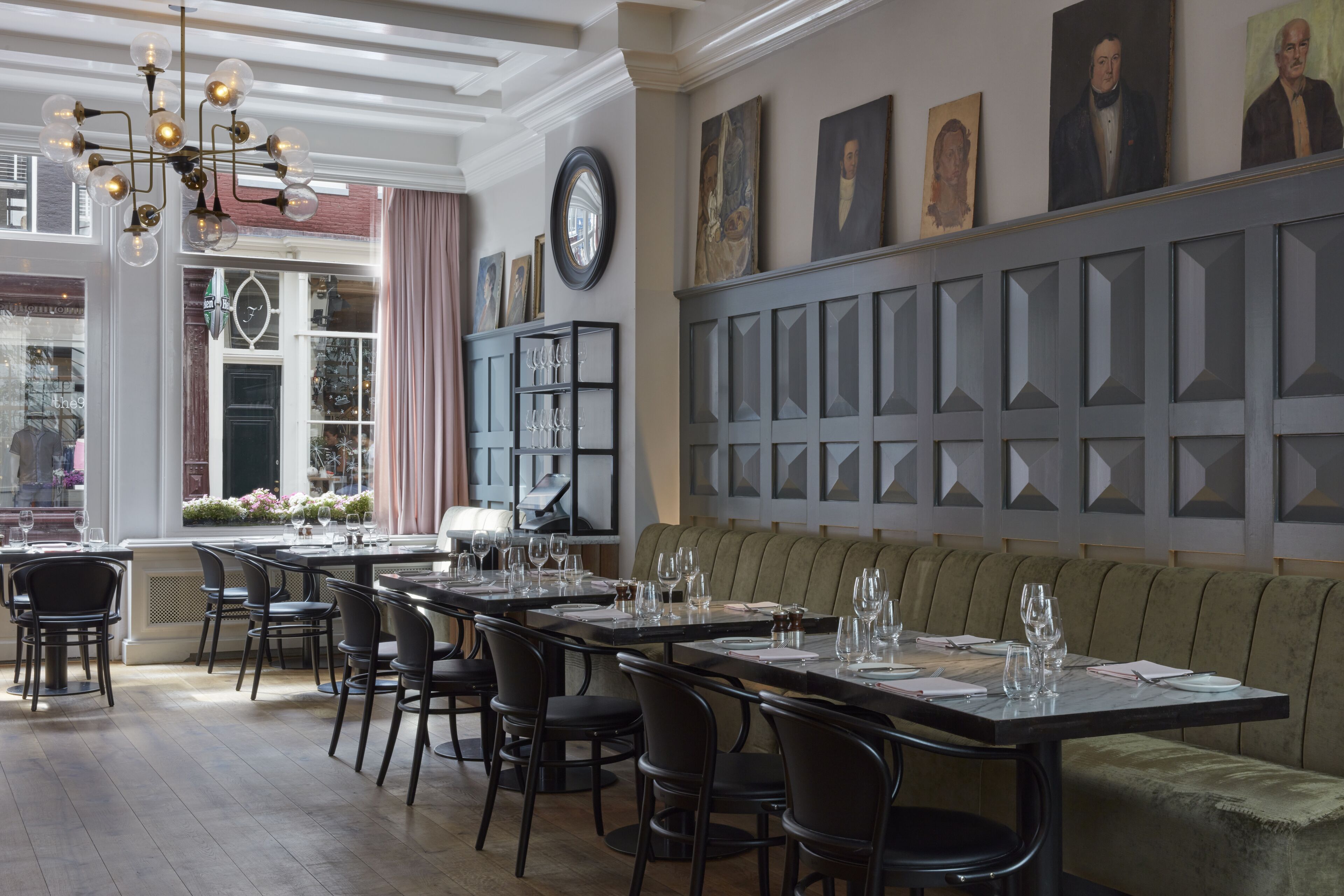 Ein Restaurant mit langen Tischen, Stühlen und einem Kronleuchter. An den Wänden befinden sich Gemälde und eine Uhr.