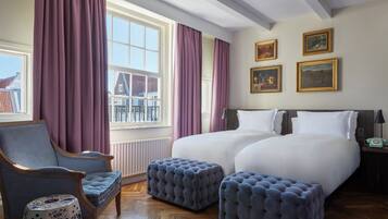 Habitación de hotel con una cama grande, dos mesitas de noche, una silla y una ventana con cortinas.