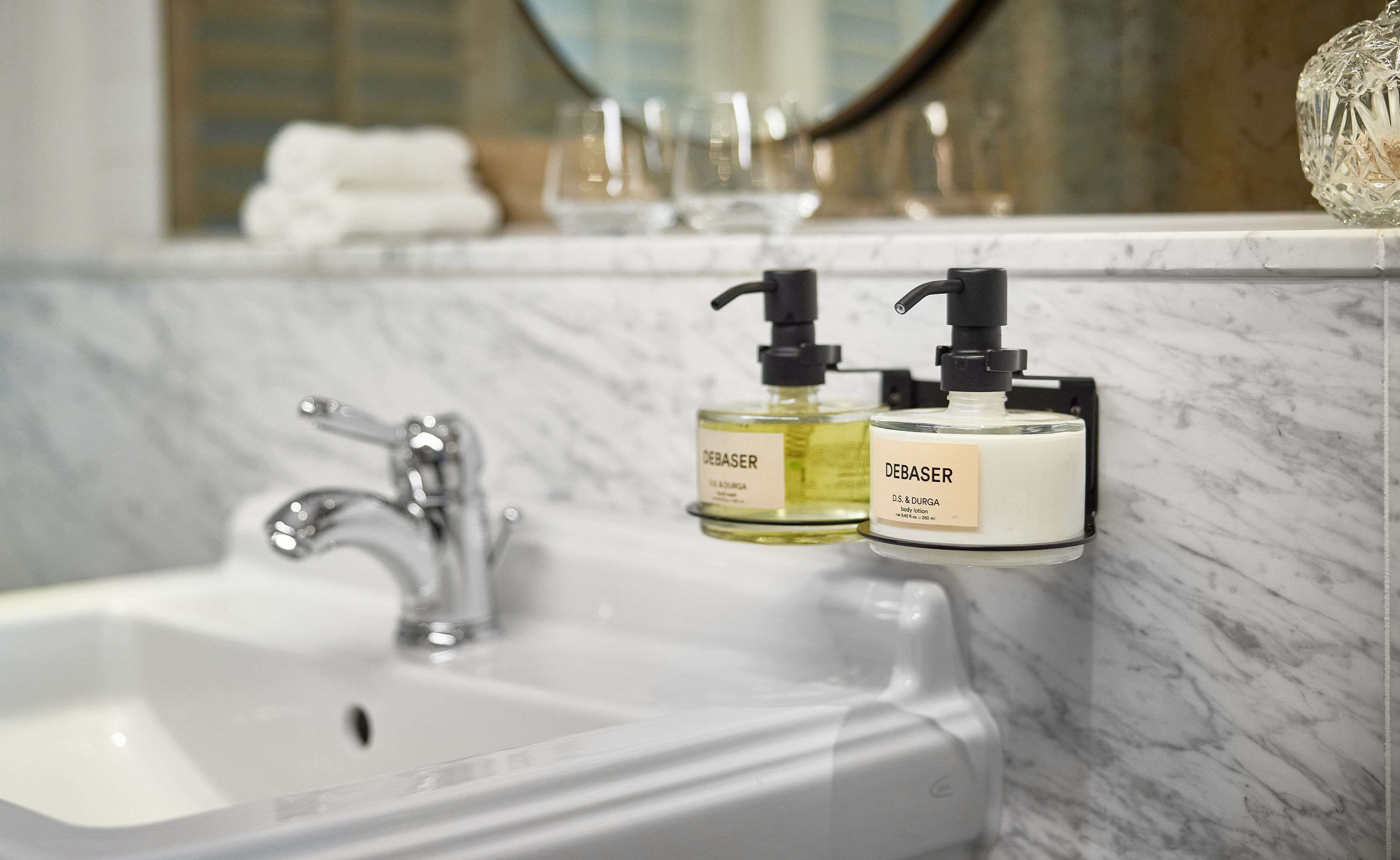 A bathroom sink with two Debaser body lotion bottles on a marble countertop.