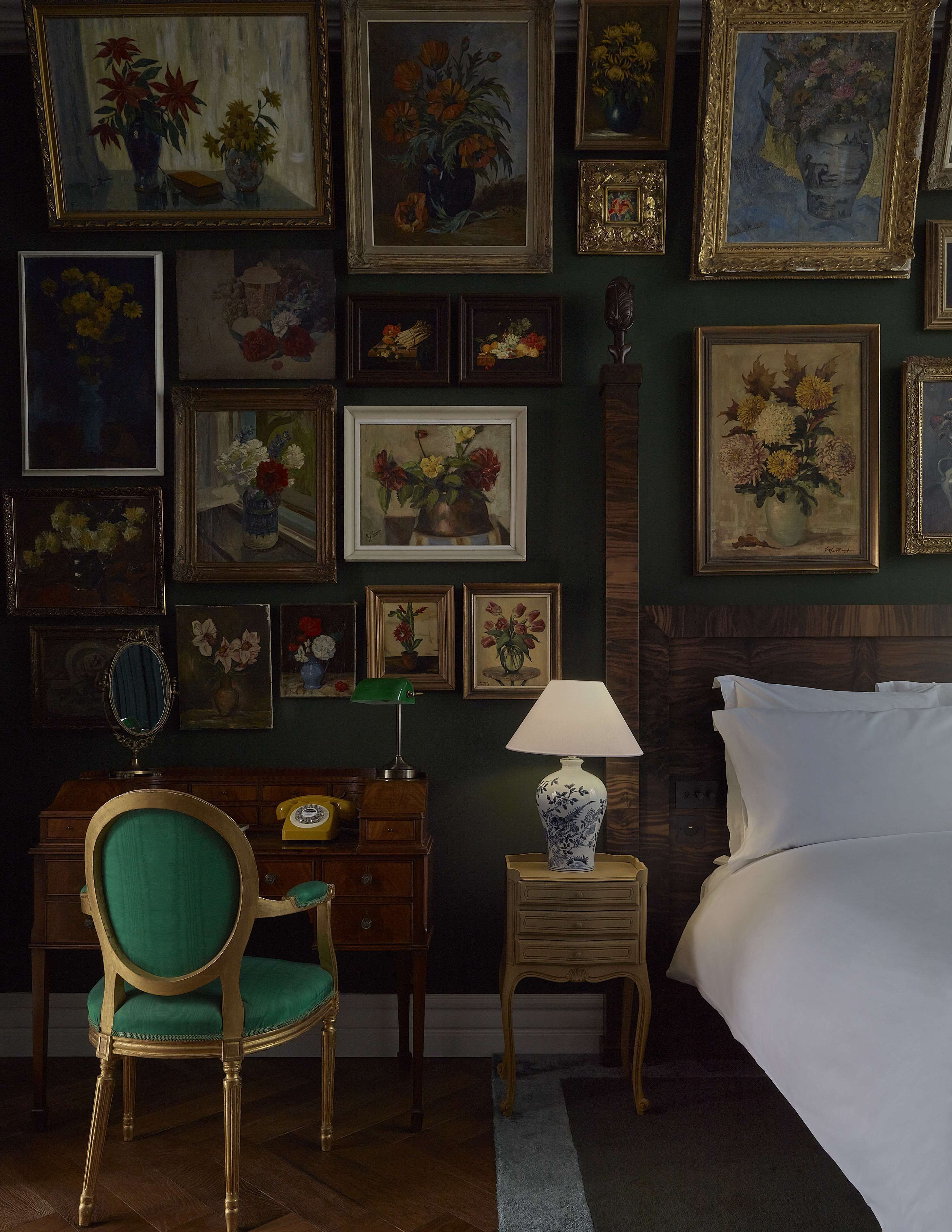 A room with a green chair, a small table with a lamp, and a bed with white linens.