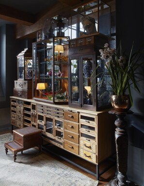 A vintage wooden cabinet with multiple drawers and glass-fronted shelves, a small wooden stool, and a potted orchid plant.