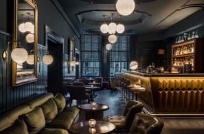 Zona de bar con mostrador, estantes llenos de botellas y asientos que incluyen un sofá y mesas redondas.