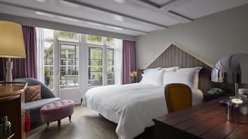 Une chambre d’hôtel avec un grand lit, un bureau en bois, une chaise, une petite table et une fenêtre avec des rideaux.