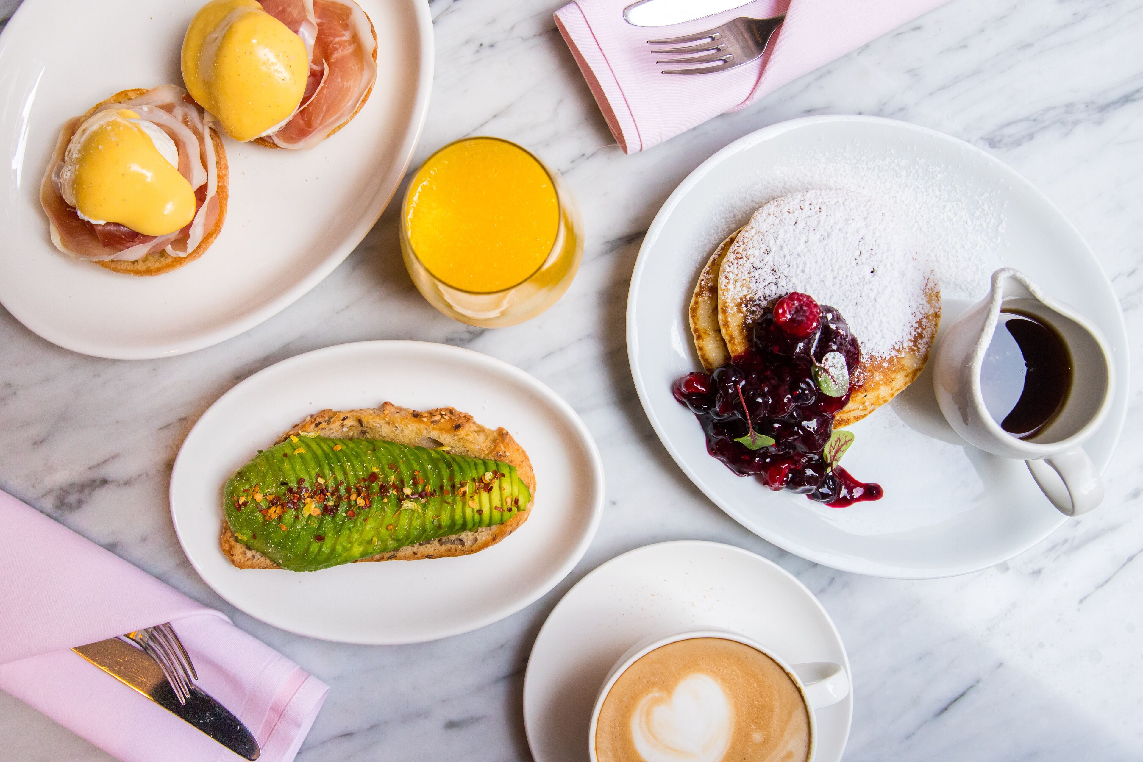 Una colazione con diversi piatti, tra cui uova, pancake con frutti di bosco, un dolce verde e una tazza di caffè.