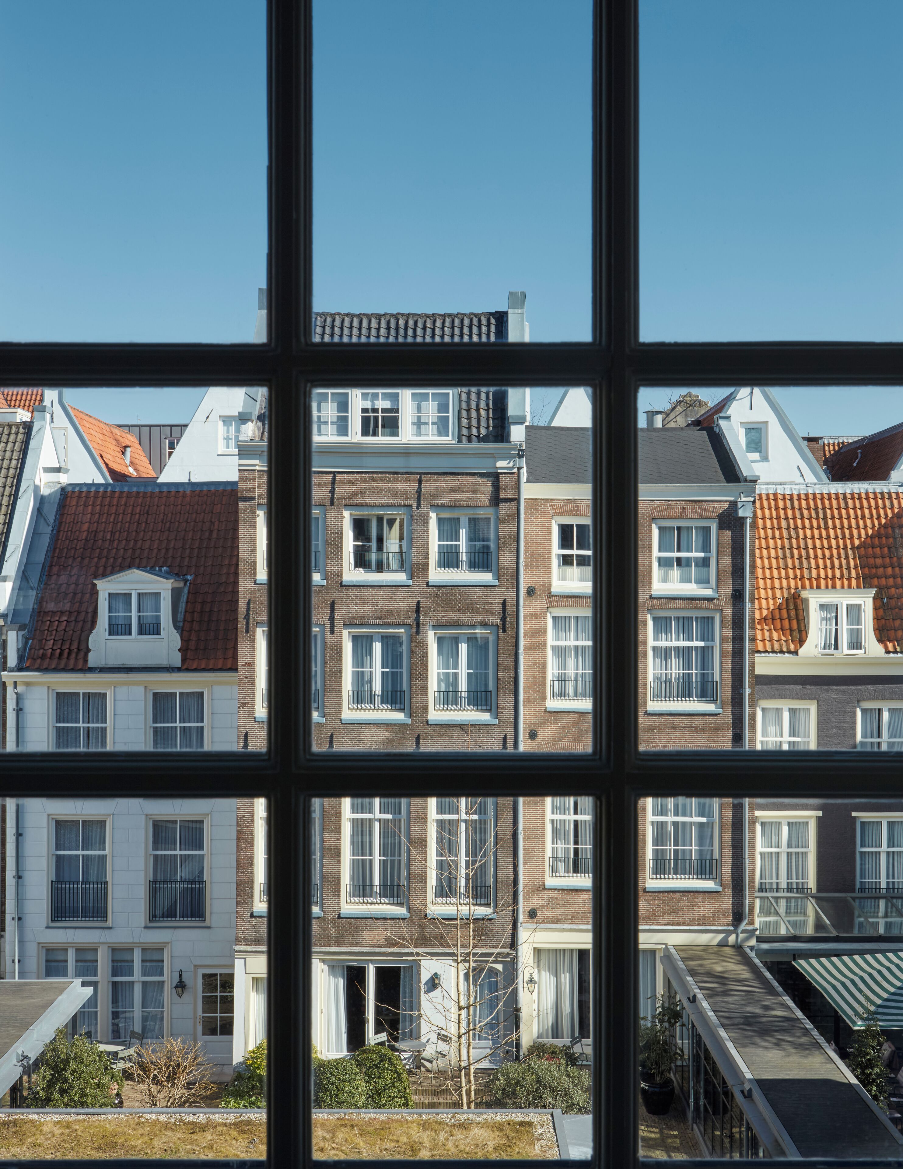 Una hilera de casas urbanas con múltiples ventanas y balcones, vista a través de un marco de ventana.