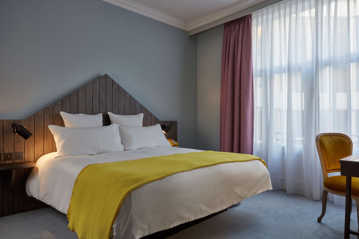Una habitación de hotel con cama, una silla, una mesita de noche y una ventana con cortinas.