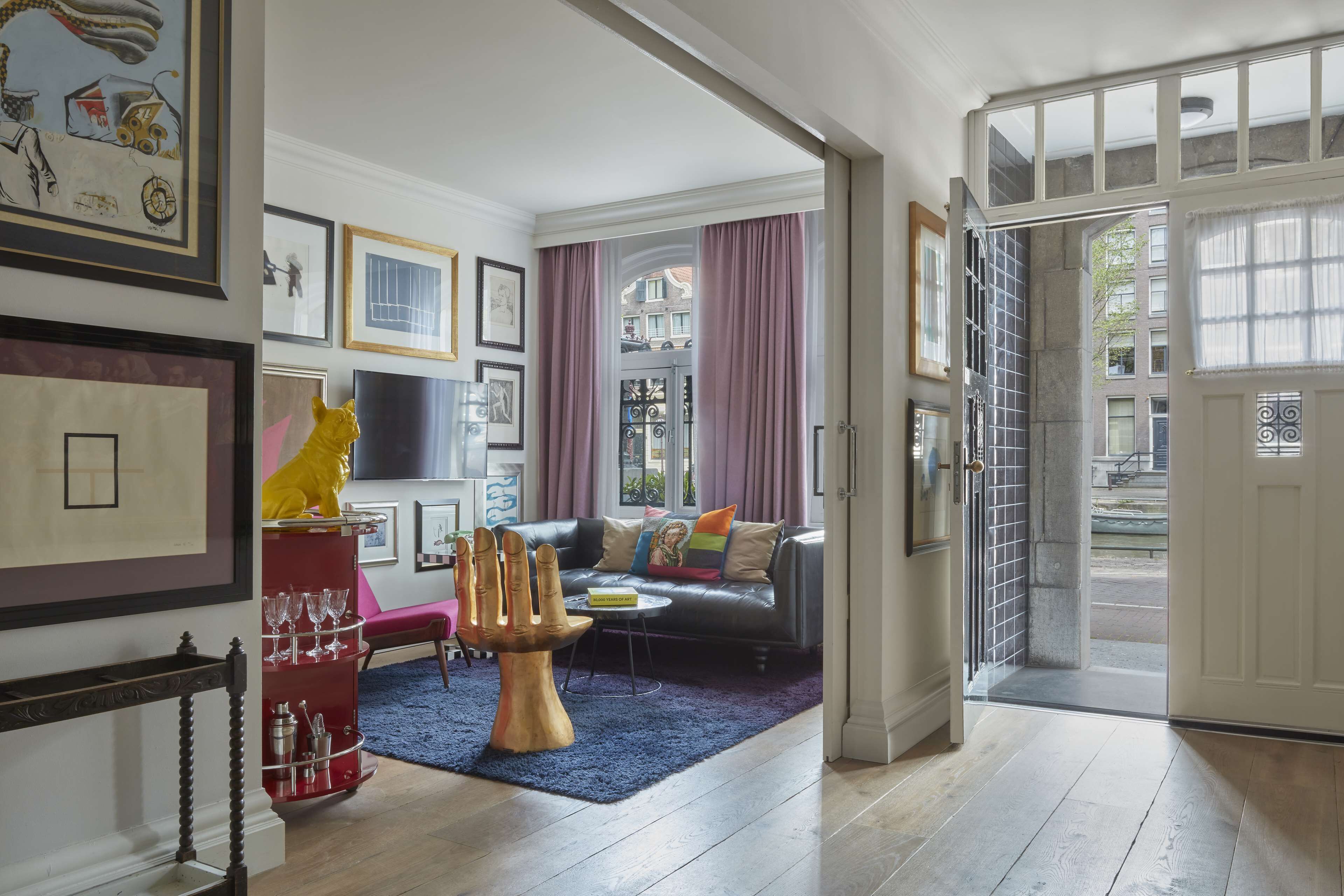 A modern living room with a sofa, a coffee table, and a unique footstool. There are framed pictures on the wall and a red cabinet with glassware.
