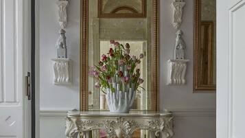 A white console table with a vase of flowers, flanked by two wall-mounted sculptures, in a room with a large mirror and ornate ceiling.