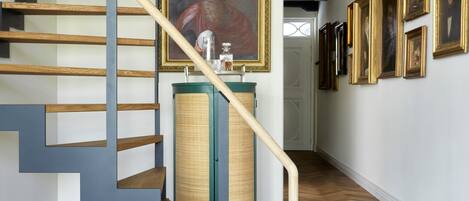Una escalera con escalones de madera y barandilla azul, que conduce a una habitación con un cuadro grande y un armario verde.