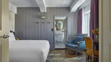 A hotel room with a bed, a chair, a desk, a mirror, and a bathroom with a sink and shower.