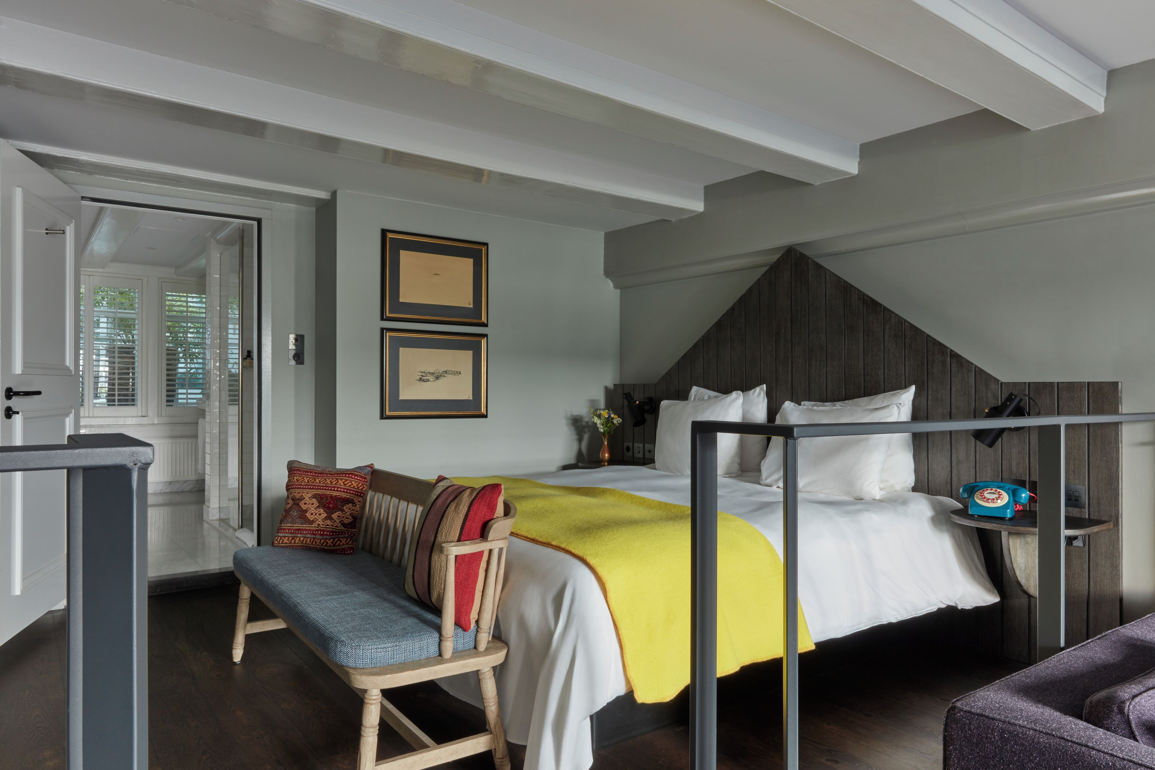 A bedroom with a bed, a bench, a bedside table, and a door leading to another room.
