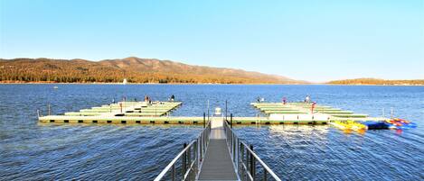 Un muelle que conduce a muelles flotantes con barcos y un telón de fondo montañoso.