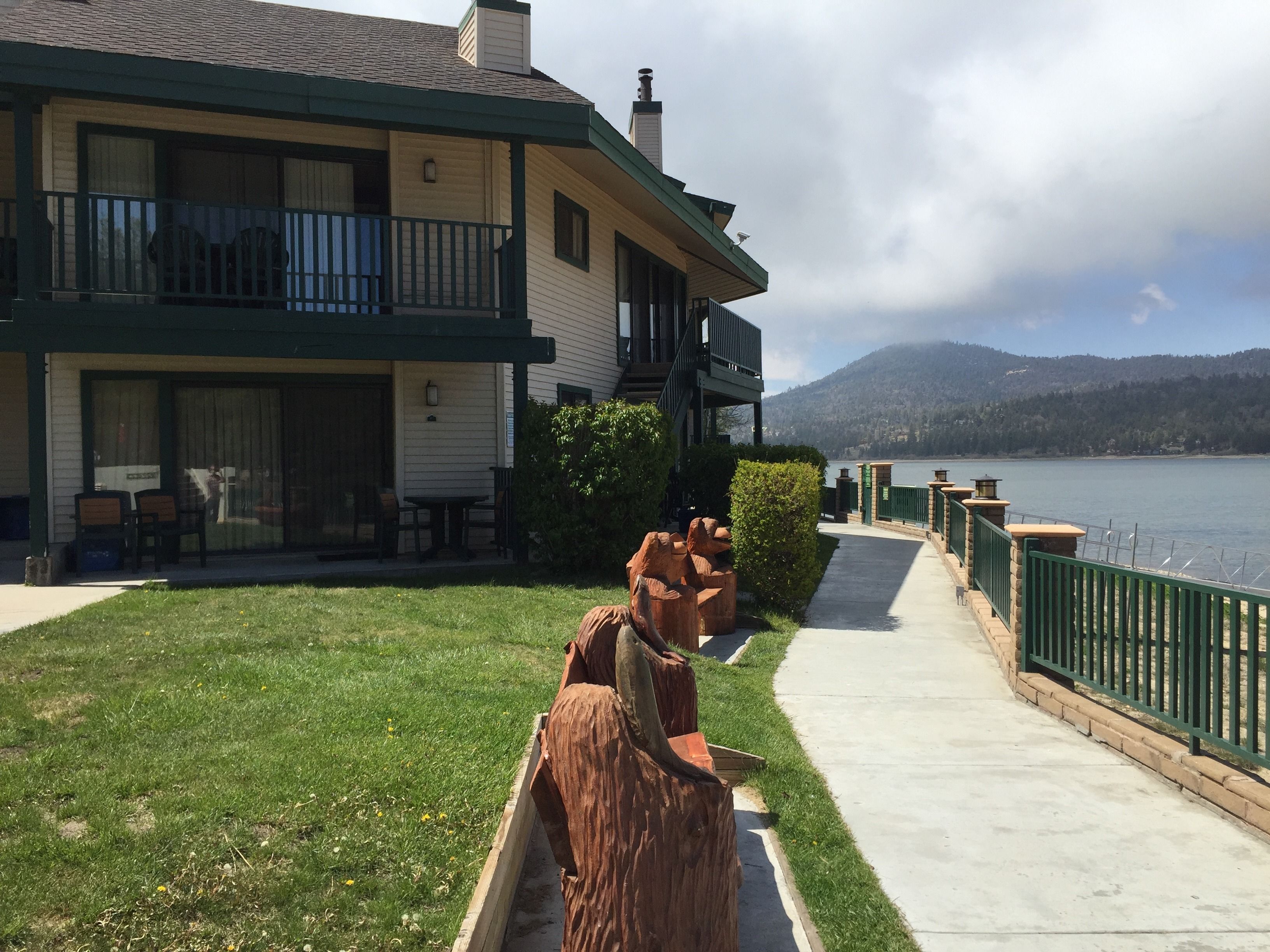 A hotel with a covered outdoor seating area, a pathway leading to a body of water, and a view of mountains in the distance.