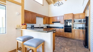 Eine Küche mit Holzausstattung, einer zentralen Kochinsel mit Barhocker, einem Einbauofen und einem Kühlschrank.